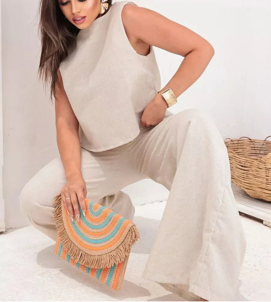 Mulher com conjunto bege de linho, segurando bolsa de palha colorida com franjas, moda verão elegante.