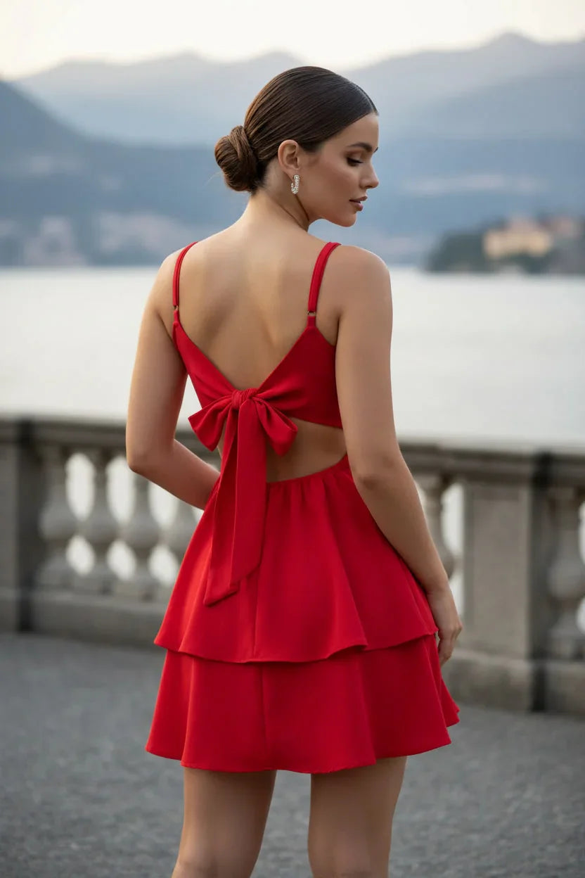 Mulher elegante de costas usando vestido vermelho curto com laço, vista para lago ao fundo.