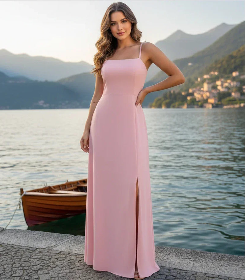 Mulher com vestido longo rosa claro elegante, alça fina, fenda lateral, à beira de lago.